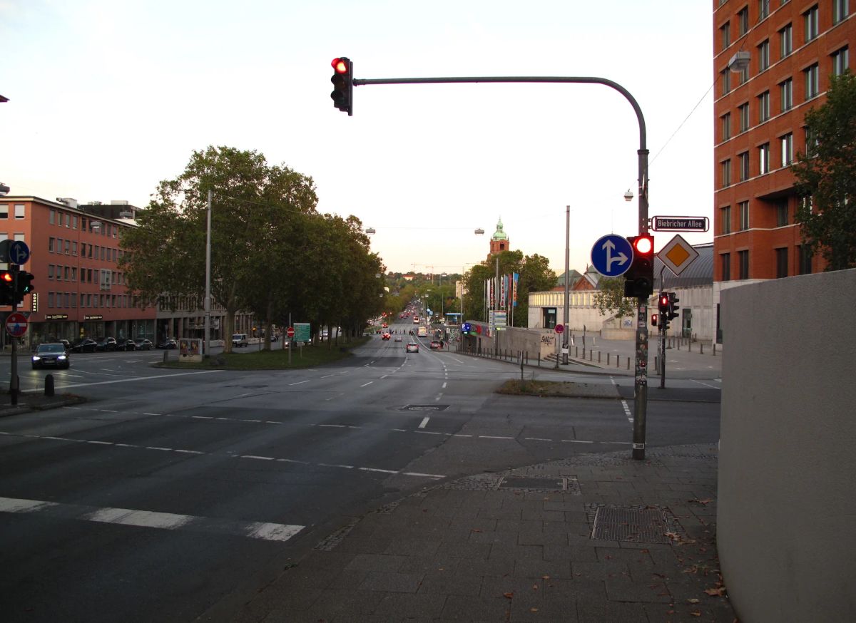 Ampelkreuzung an der Biebricher Allee in Wiesbaden in der Abenddämmerung, die Ampeln zeigen Rot, dahinter eine mehrspurige Allee mit Autos in der Ferne.