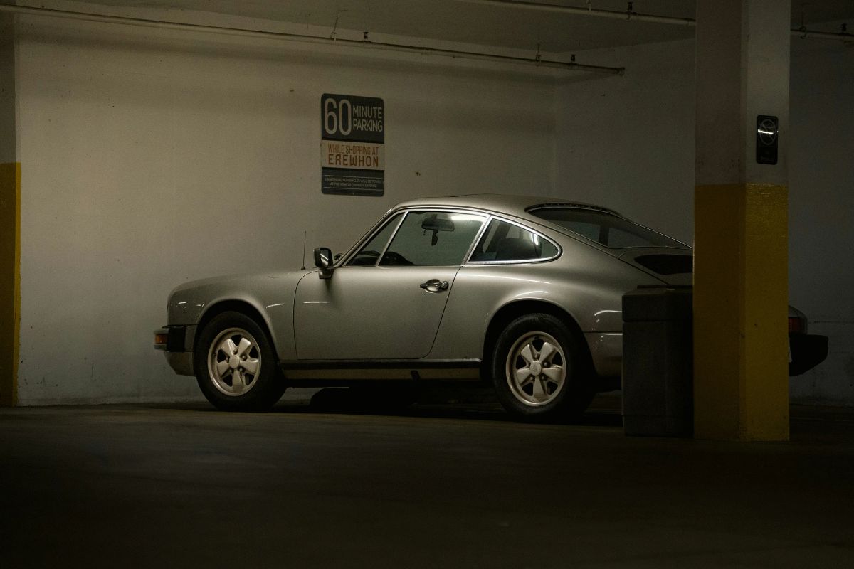 Silbernes Oldtimer-Coupé steht seitlich in einem schwach beleuchteten Parkhaus.