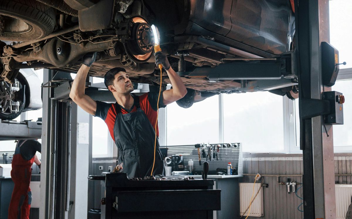 Mechaniker leuchtet mit einer Handlampe die Bremsscheibe und das Fahrwerk eines Autos auf der Hebebühne aus.
