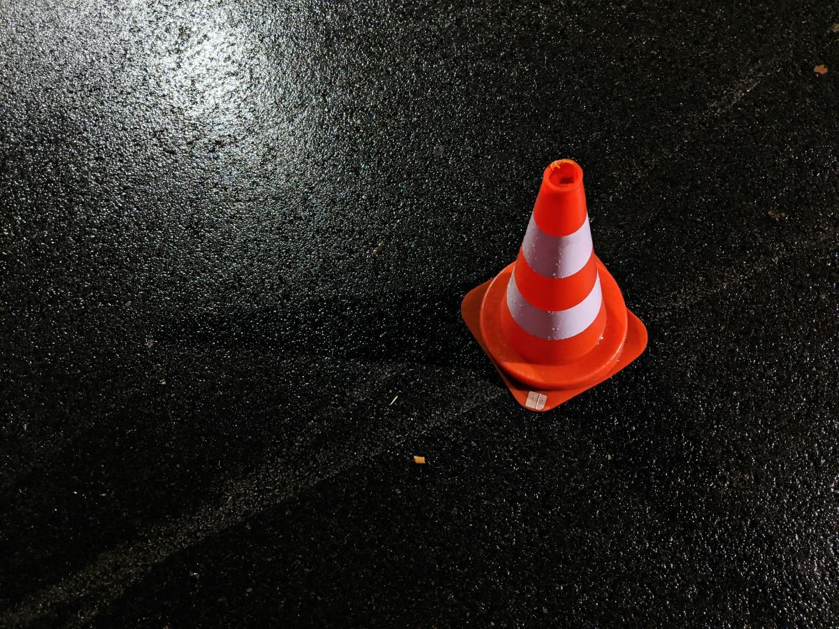 Warnkegel auf nassem Asphalt bei Nacht, im Hintergrund unscharfe Lichter